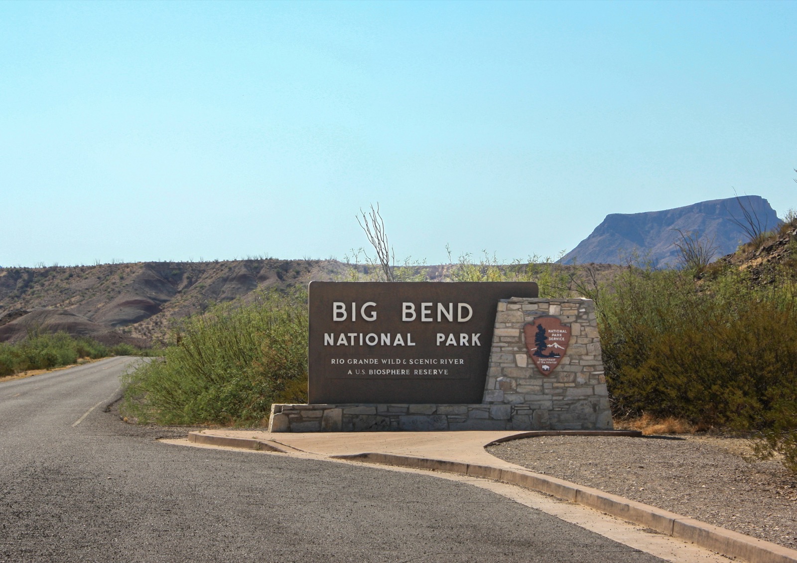 Construction vehicles and equipment on a remote desert road near Big Bend National Park, with mountains in the background under a clear sky.